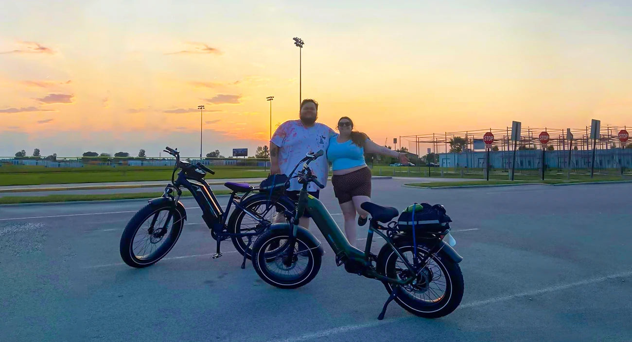 Is There a Weight Limit on Ebikes? Two people are posing with their electric bikes at sunset in a parking lot near a sports field.