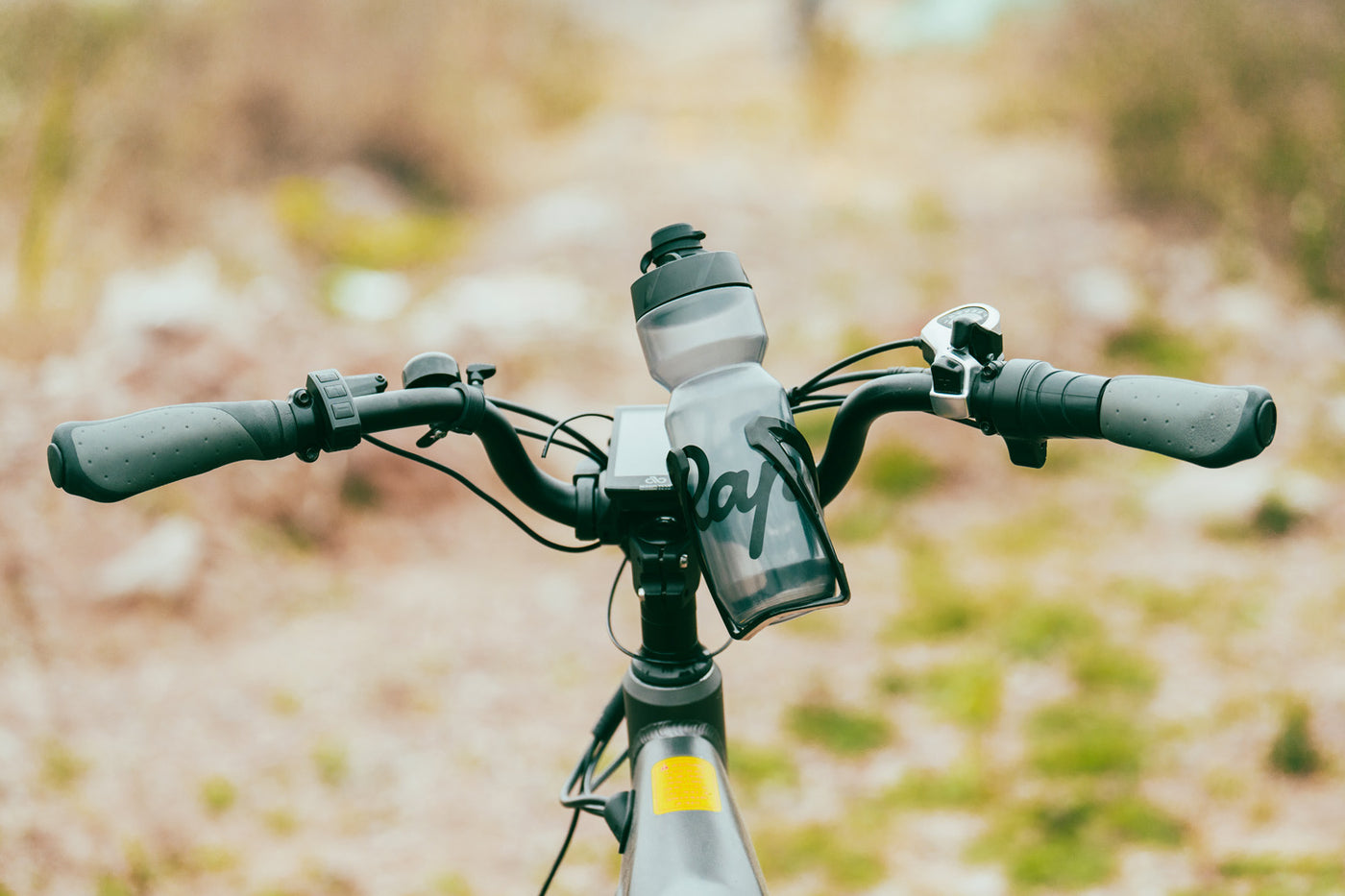 Bike handlebars with adjustable water bottle holder and bottle on a scenic trail