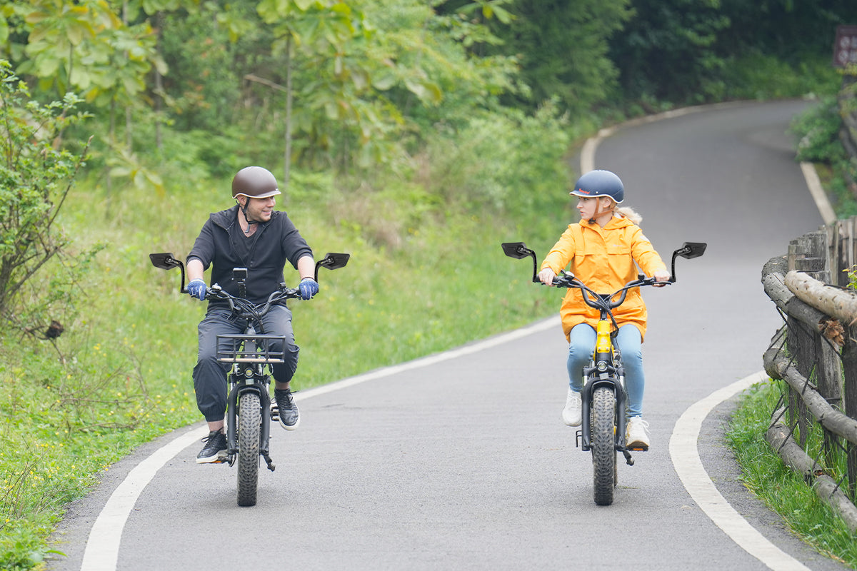 Riders on electric bikes using adjustable rearview mirrors on a forest path.