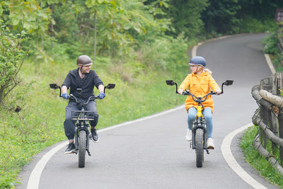 Riders on electric bikes using adjustable rearview mirrors on a forest path.