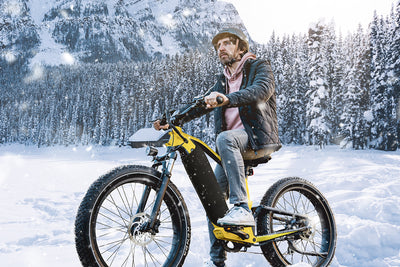 Man riding yellow electric bike in snowy mountains, perfect for winter adventures.