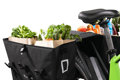 Spacious black cargo pannier bags filled with fresh produce on a bicycle.