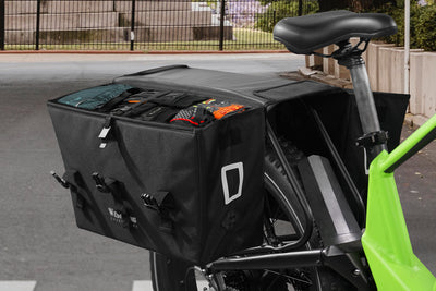 Large black bicycle cargo pannier bag filled with tools on electric bike rack.